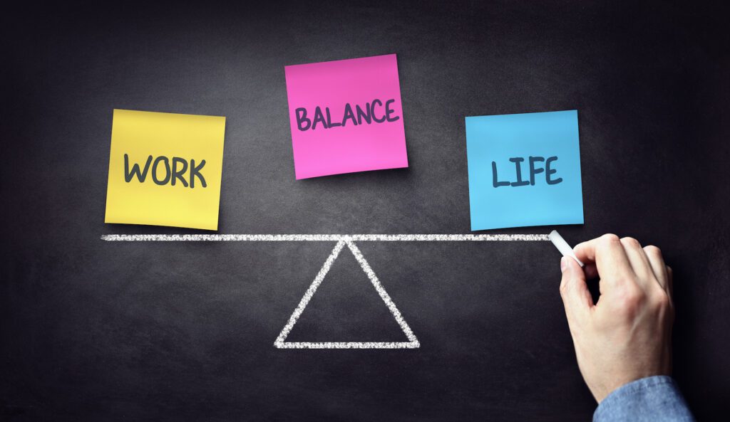 Work, Balance, and Life on a Yellow, Pink and Blue sticky note. Black background with lighting effect and a trianfle balance beam shocasing the delicate balance between the three items for non-degree seeking students